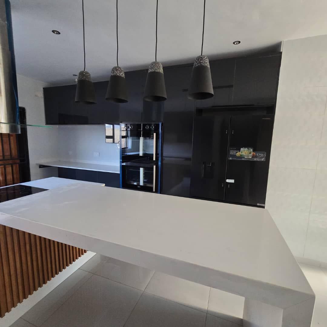 Black gloss kitchen with a white quartz waterfall island and pendant lighting.