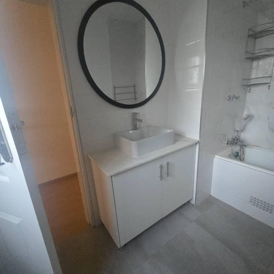 Compact white vanity unit with a counter-top basin and a round black-framed mirror.
