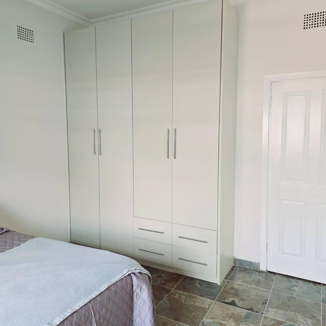 Floor-to-ceiling cream fitted wardrobe run with a drawer bank in a bedroom.