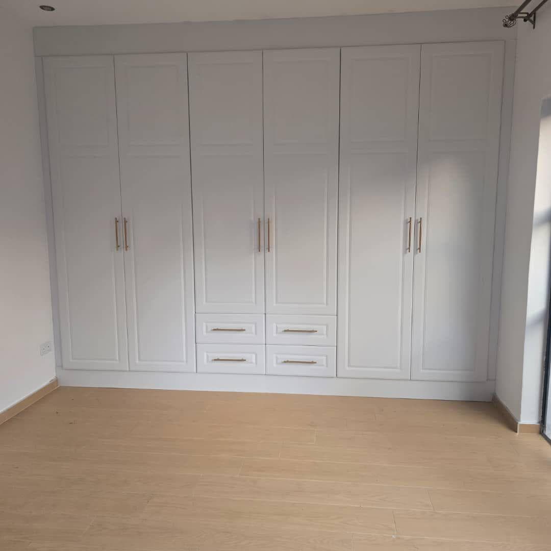 Full-wall white panelled fitted wardrobes with brushed brass bar handles.